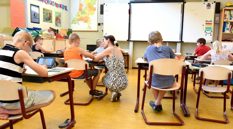 Enseignante aidant un élève dans une classe réaménagée avec des élèves concentrés sur leurs activités.