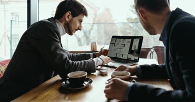 Deux hommes en réunion autour d’un ordinateur portable avec des tasses de café, en train de discuter d’un projet.