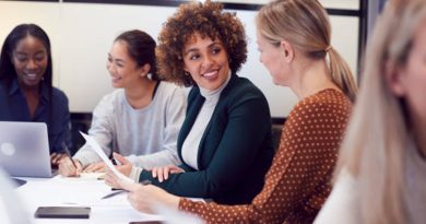 Des collègues de différentes origines discutent et sourient autour d’une table de réunion, dans un environnement de travail collaboratif.