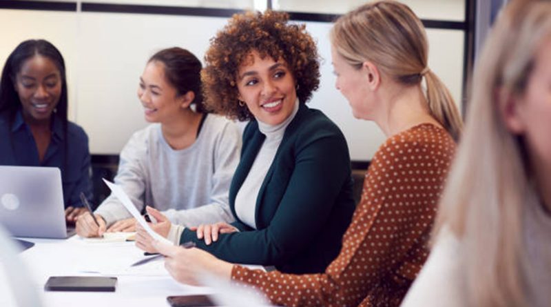 Des collègues de différentes origines discutent et sourient autour d’une table de réunion, dans un environnement de travail collaboratif.