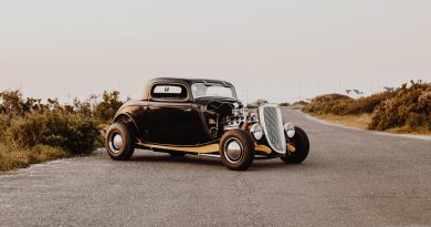 Voiture de collection noire et dorée garée sur une route de campagne, avec son moteur apparent, au coucher du soleil.