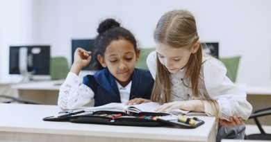 Deux jeunes filles assises à un bureau en classe, regardant un livre ouvert ensemble et travaillant côte à côte.