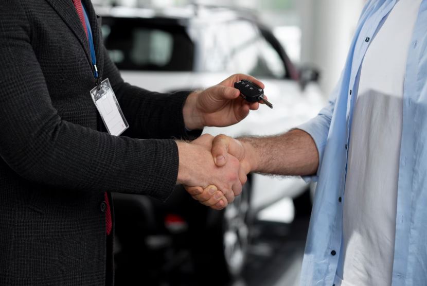 Un vendeur remet les clés d’une voiture à un acheteur tout en lui serrant la main dans une concession automobile