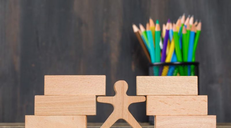 Figurine en bois entre deux piles de blocs avec des crayons de couleur en arrière-plan