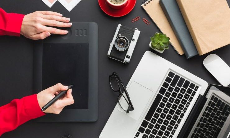 Poste de travail de graphiste avec tablette graphique, ordinateur portable, appareil photo et accessoires créatifs sur un bureau noir