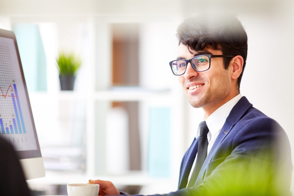 Homme souriant en costume bleu analysant des graphiques sur son écran
