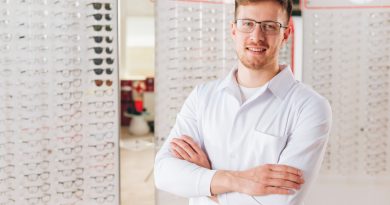Jeune opticien en blouse blanche posant devant des présentoirs de lunettes