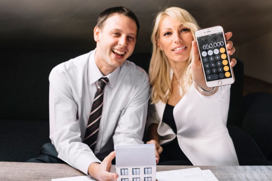 Conseillers présentant une maquette de maison et un résultat chiffré sur smartphone.