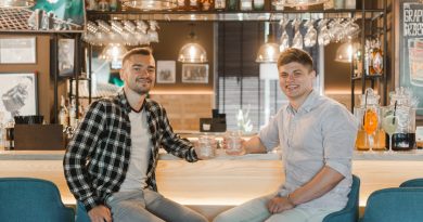 Deux jeunes hommes souriants sont assis au comptoir d'un bar tenant chacun un verre à la main