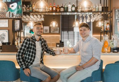 Deux jeunes hommes souriants sont assis au comptoir d'un bar tenant chacun un verre à la main