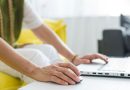 une femme utilisant une souris et le clavier d'un ordinateur portable posé sur une table blanche