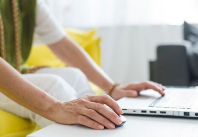 une femme utilisant une souris et le clavier d'un ordinateur portable posé sur une table blanche