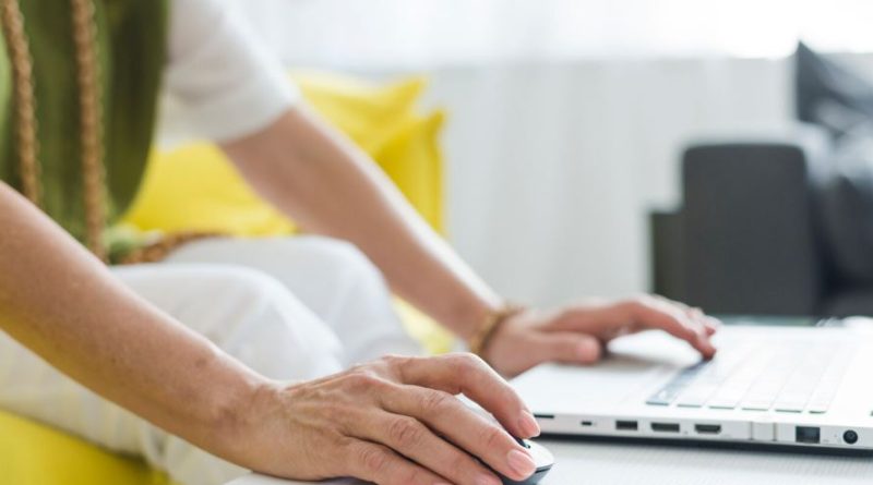 une femme utilisant une souris et le clavier d'un ordinateur portable posé sur une table blanche