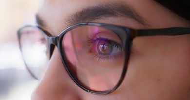 œil d'une femme portant des lunettes de vue à monture noire avec des reflets roses et violets sur les verres