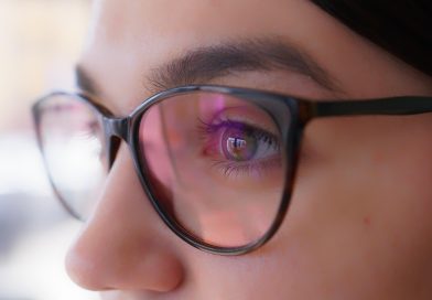œil d'une femme portant des lunettes de vue à monture noire avec des reflets roses et violets sur les verres
