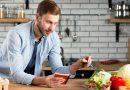 Un homme dans une cuisine note soigneusement ses courses dans un carnet tout en examinant des légumes frais posés sur le plan de travail