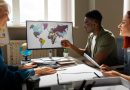 Trois collègues de bureau discutent d'une stratégie internationale devant un écran affichant une carte du monde colorée
