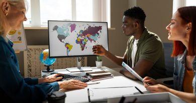 Trois collègues de bureau discutent d'une stratégie internationale devant un écran affichant une carte du monde colorée