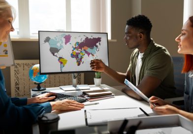 Trois collègues de bureau discutent d'une stratégie internationale devant un écran affichant une carte du monde colorée