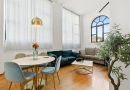 Un salon lumineux au style contemporain avec une table à manger ronde, un canapé en velours bleu canard, un canapé gris et une grande fenêtre en arche