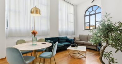 Un salon lumineux au style contemporain avec une table à manger ronde, un canapé en velours bleu canard, un canapé gris et une grande fenêtre en arche