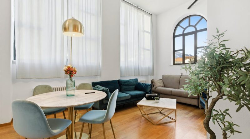 Les nouvelles tendances de la gestion locative meublée à Paris en 2026 Un salon lumineux au style contemporain avec une table à manger ronde, un canapé en velours bleu canard, un canapé gris et une grande fenêtre en arche