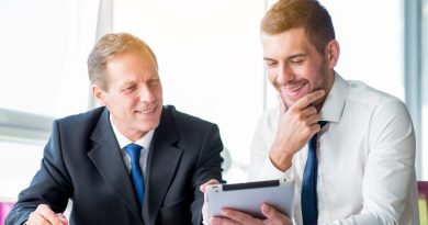 Deux conseillers financiers en costume sourient en regardant ensemble une tablette numérique dans un bureau lumineux.