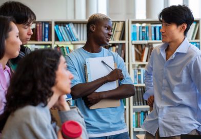 un groupe d'étudiants d'origines diverses échangeant de manière vivante et décontractée au milieu des étagères d'une bibliothèque.