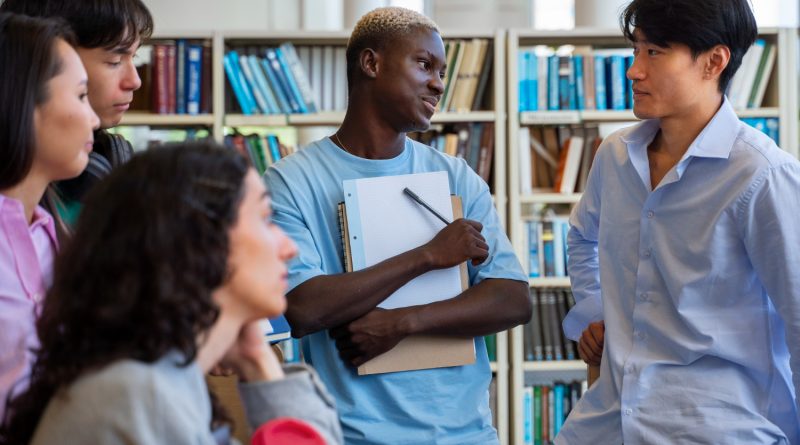 un groupe d'étudiants d'origines diverses échangeant de manière vivante et décontractée au milieu des étagères d'une bibliothèque.