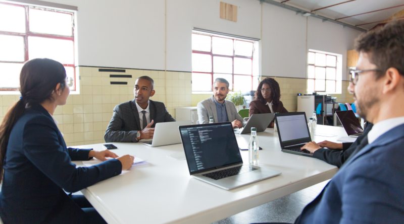 une équipe de professionnels réunis autour d'une grande table avec leurs ordinateurs portables lors d'une réunion de travail dans un espace lumineux