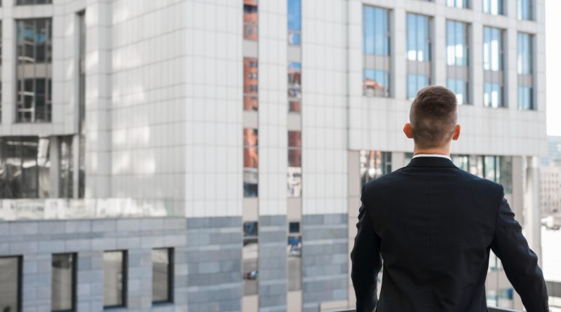 Joris Dutel : un parcours de direction construit au cœur des marchés africains un homme d'affaires vu de dos, vêtu d'un costume sombre, contemplant des immeubles modernes depuis un balcon