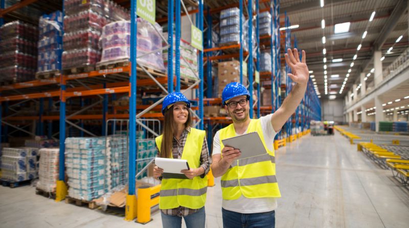 Next Terra International avis : pourquoi les entreprises choisissent un partenaire logistique spécialisé ? deux agents logistiques portant des casques de chantier bleus et des gilets jaunes haute visibilité dans un grand entrepôt