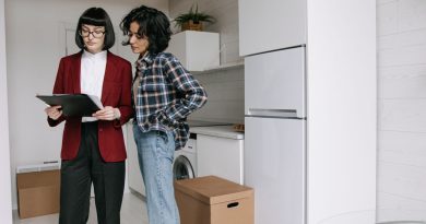 une agente immobilière en veste rouge examinant des documents sur un porte-bloc avec une cliente dans une cuisine moderne en plein déménagement.