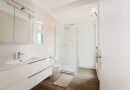 une salle de bain moderne et lumineuse dotée d'un meuble vasque blanc, de toilettes suspendues, d'une cabine de douche vitrée et d'un parquet effet bois.
