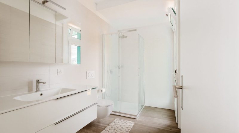 Tapis de bain La Berge : avis, confort et qualité, que pensent réellement les utilisateurs ? une salle de bain moderne et lumineuse dotée d'un meuble vasque blanc, de toilettes suspendues, d'une cabine de douche vitrée et d'un parquet effet bois.