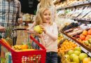 Une petite fille souriante tenant un fruit dans un rayon de supermarché aux côtés de ses parents.