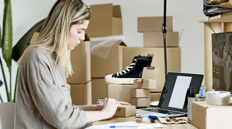 Une femme préparant des colis et gérant des commandes devant son ordinateur portable dans un atelier d'e-commerce