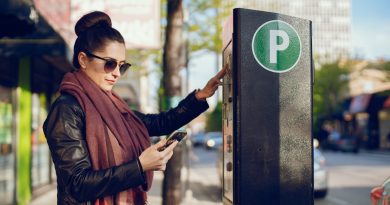 Une femme réglant son stationnement à un horodateur tout en tenant son téléphone.