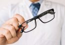 Un opticien en blouse blanche tend une paire de lunettes de vue à monture noire rectangulaire vers l'avant.
