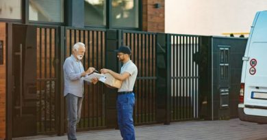 Un livreur remet un colis à un client âgé qui signe le bon de livraison devant sa maison, près d'une camionnette blanche stationnée dans la rue