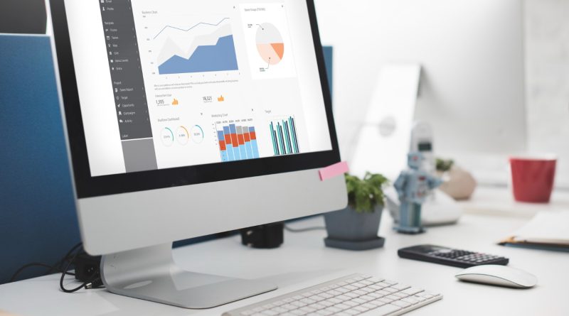 Un écran d'ordinateur de bureau affiche un tableau de bord analytique comportant divers graphiques et diagrammes commerciaux, installé sur un travail de bureau moderne et épuré avec un clavier, une souris et une calculatrice.